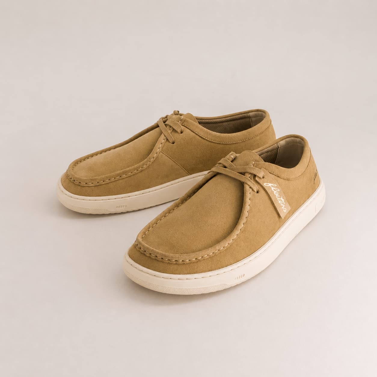 A pair of tan suede boat shoes with white soles, displayed on a light gray studio background. The brand name 'Fleeters' is visible on a small side tag.