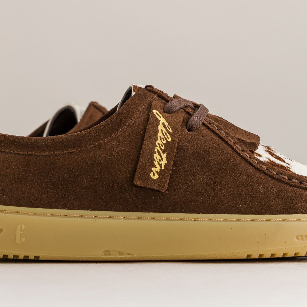 Brown suede barefoot derbies with a visible brand tag on a light gray background