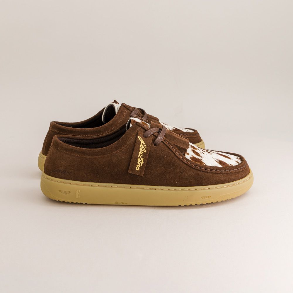 Brown suede barefoot derbies with white cow print pattern on a beige background