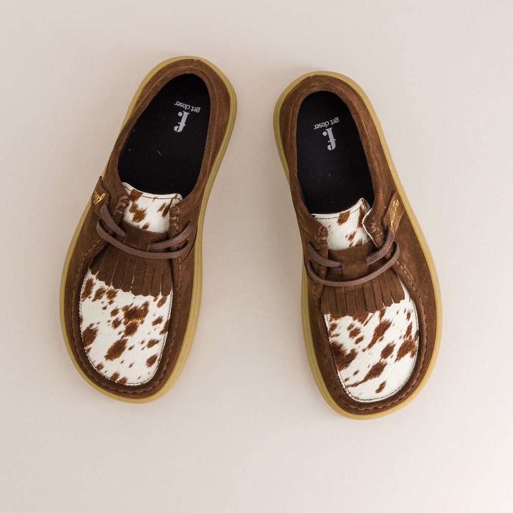 Pair of brown barefoot derbies with cow print soles on a light beige background