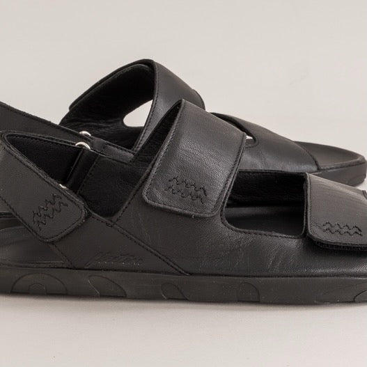 Black leather barefoot sandals with velcro straps on a light gray background