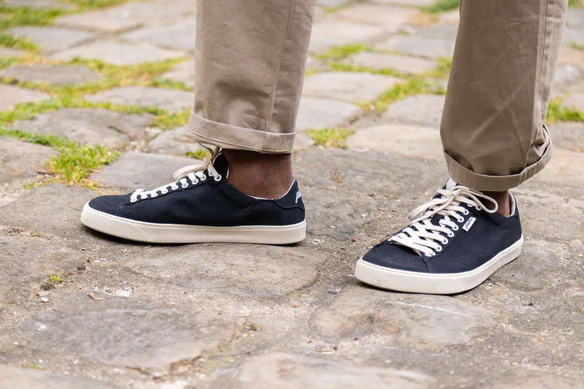 Black barefoot sneakers with white laces worn on a stone pavement.