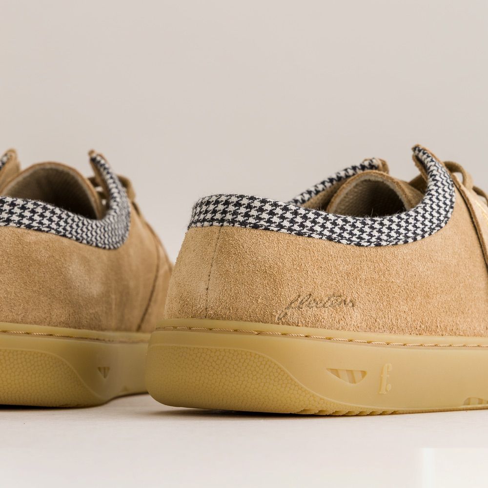 Pair of tan sneakers with houndstooth-patterned laces on a neutral background