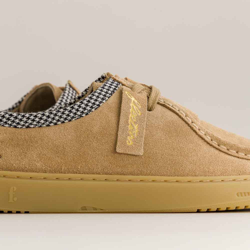 Tan barefoot shoe with a checkered tongue and brand tag on a light gray background