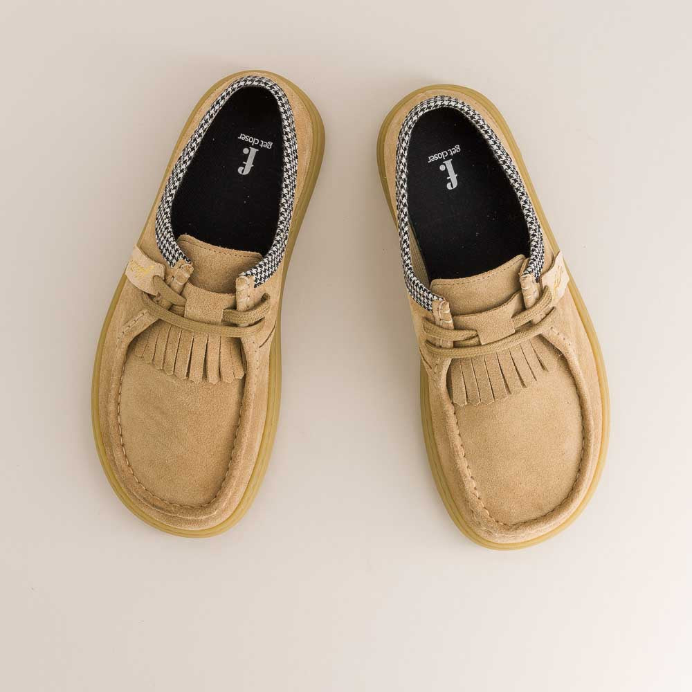 Pair of tan barefoot loafers with fringes on a light background