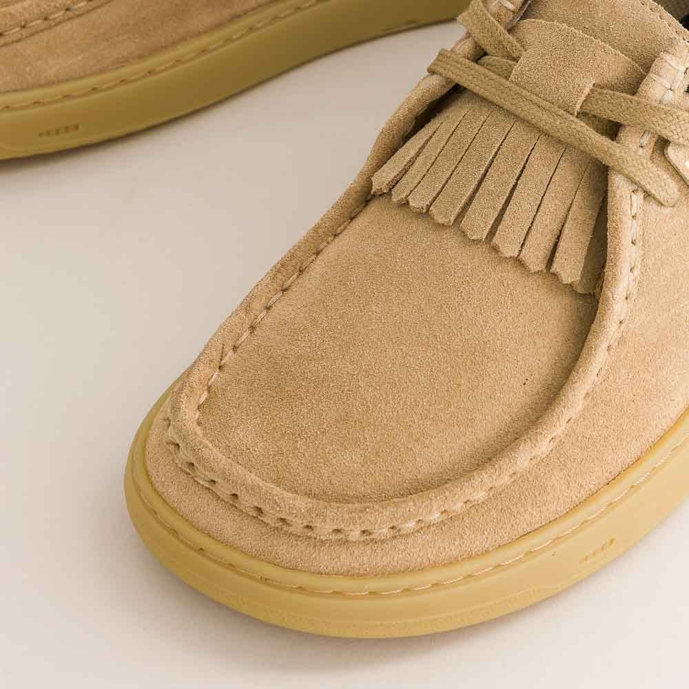 Beige suede shoe with fringes on a light background