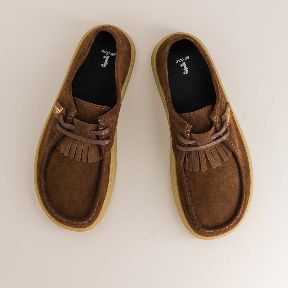 Pair of brown suede shoes with fringes on a light gray background