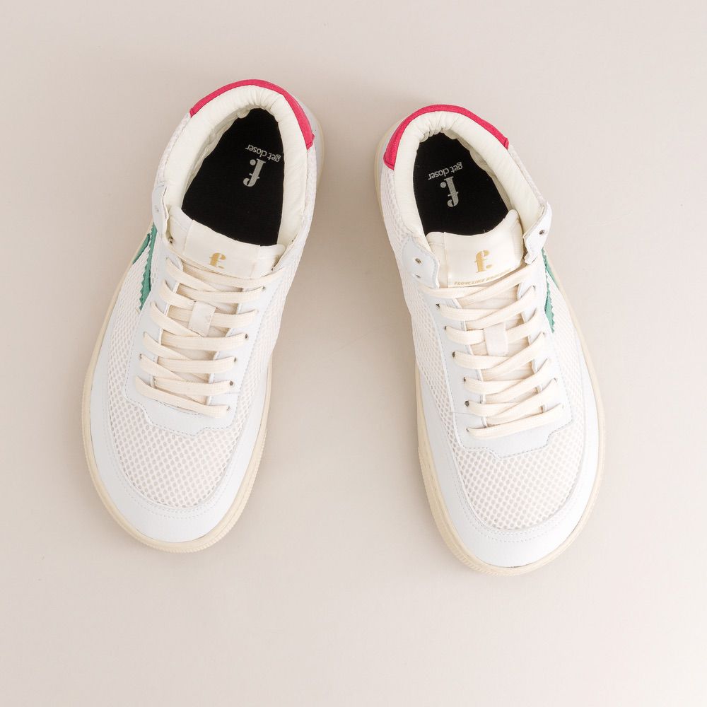 Pair of white mid-ankle barefoot sneakers with pink accents on a light beige background