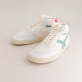 White mid-ankle barefoot sneakers with a green accent on a beige background