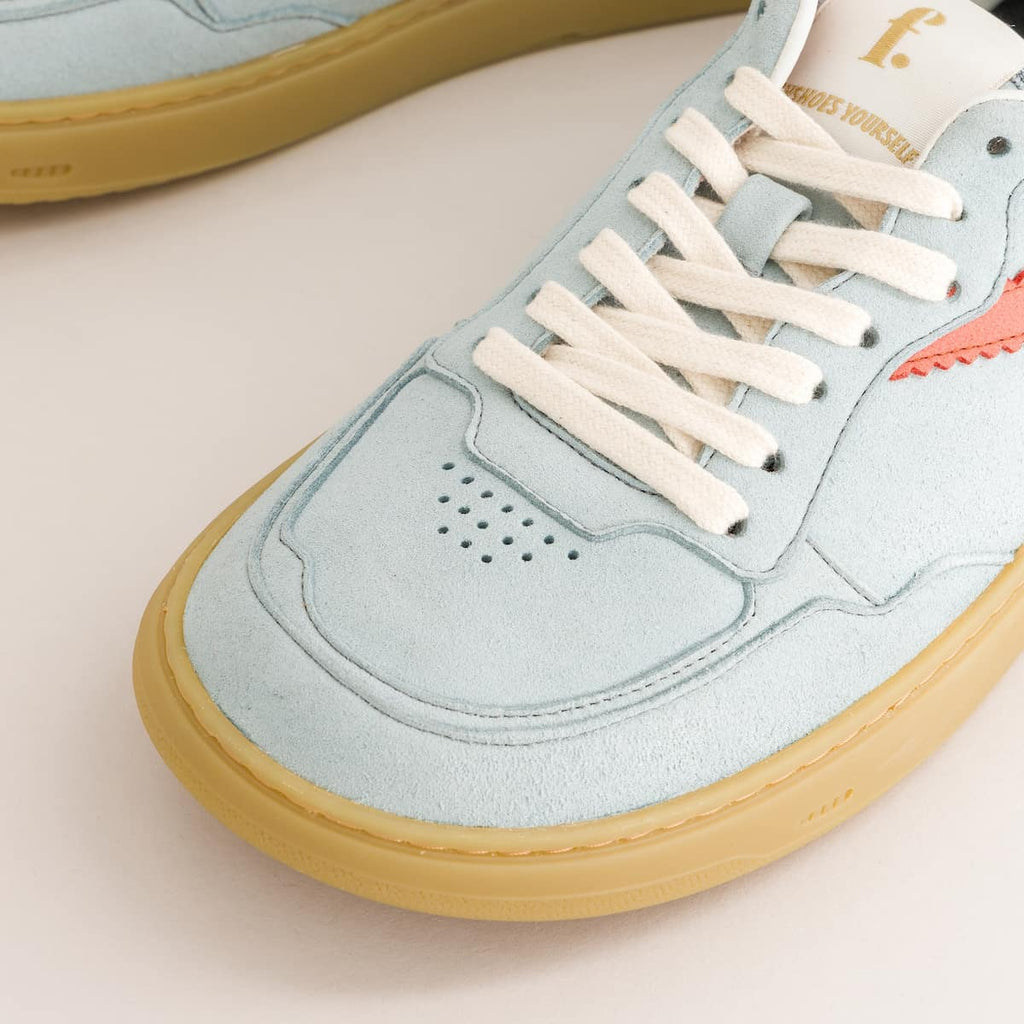 Light blue barefoot sneaker with white laces and tan sole on a beige background