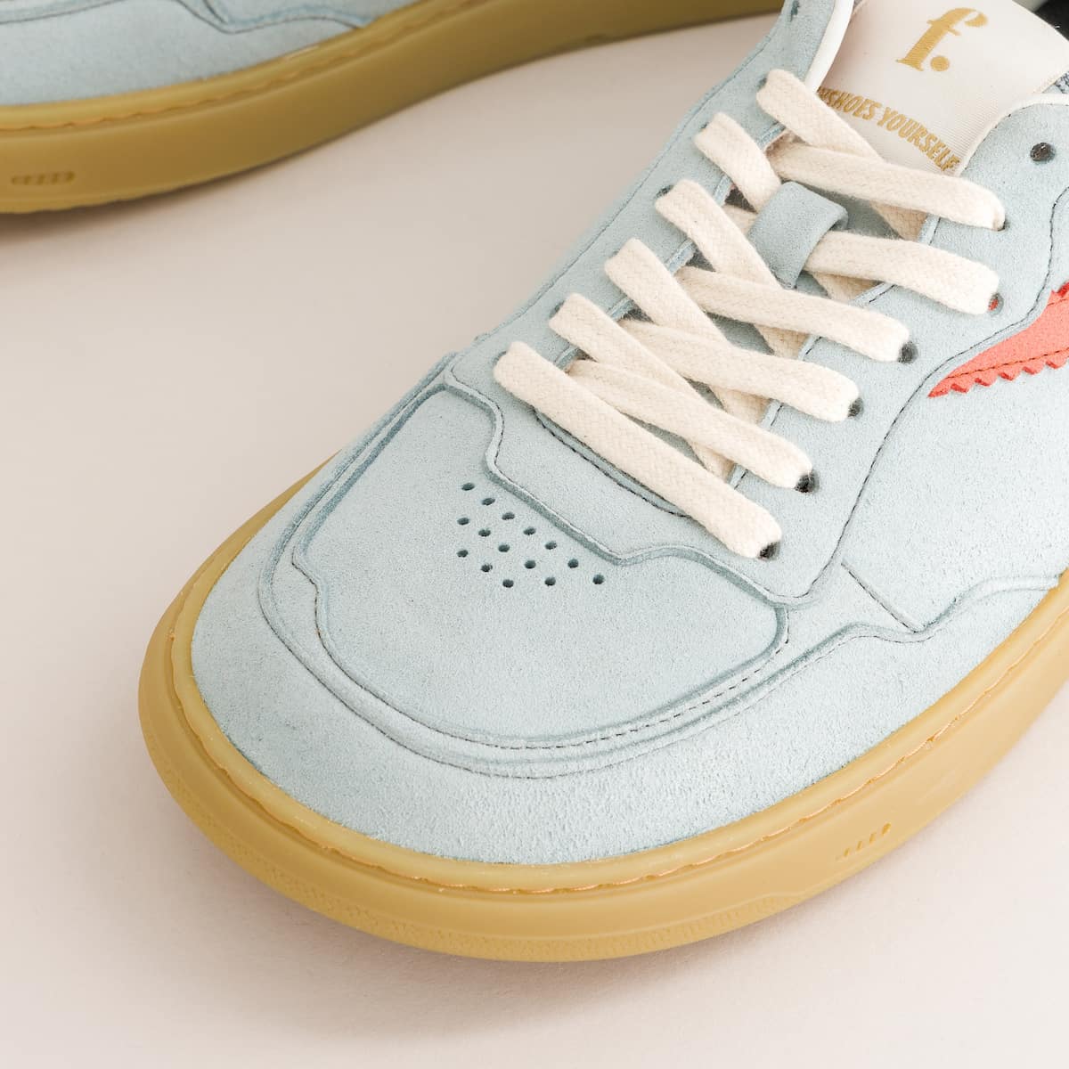 Light blue barefoot sneaker with white laces and tan sole on a beige background