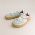 Pair of light blue barefoot sneakers with tan soles on a beige background