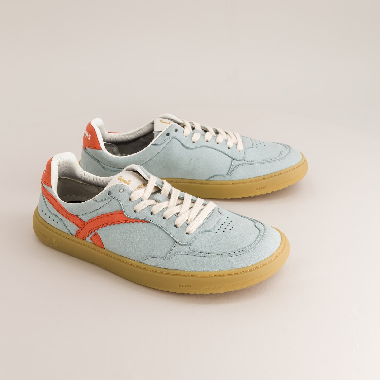 Light blue barefoot sneakers with orange accents on a beige background