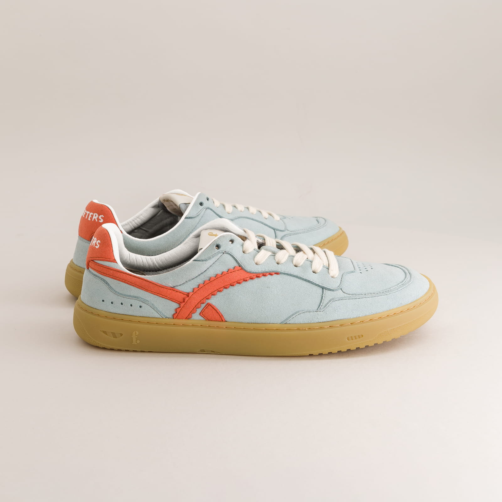Light blue barefoot sneakers with red accents and brown soles on a light gray background