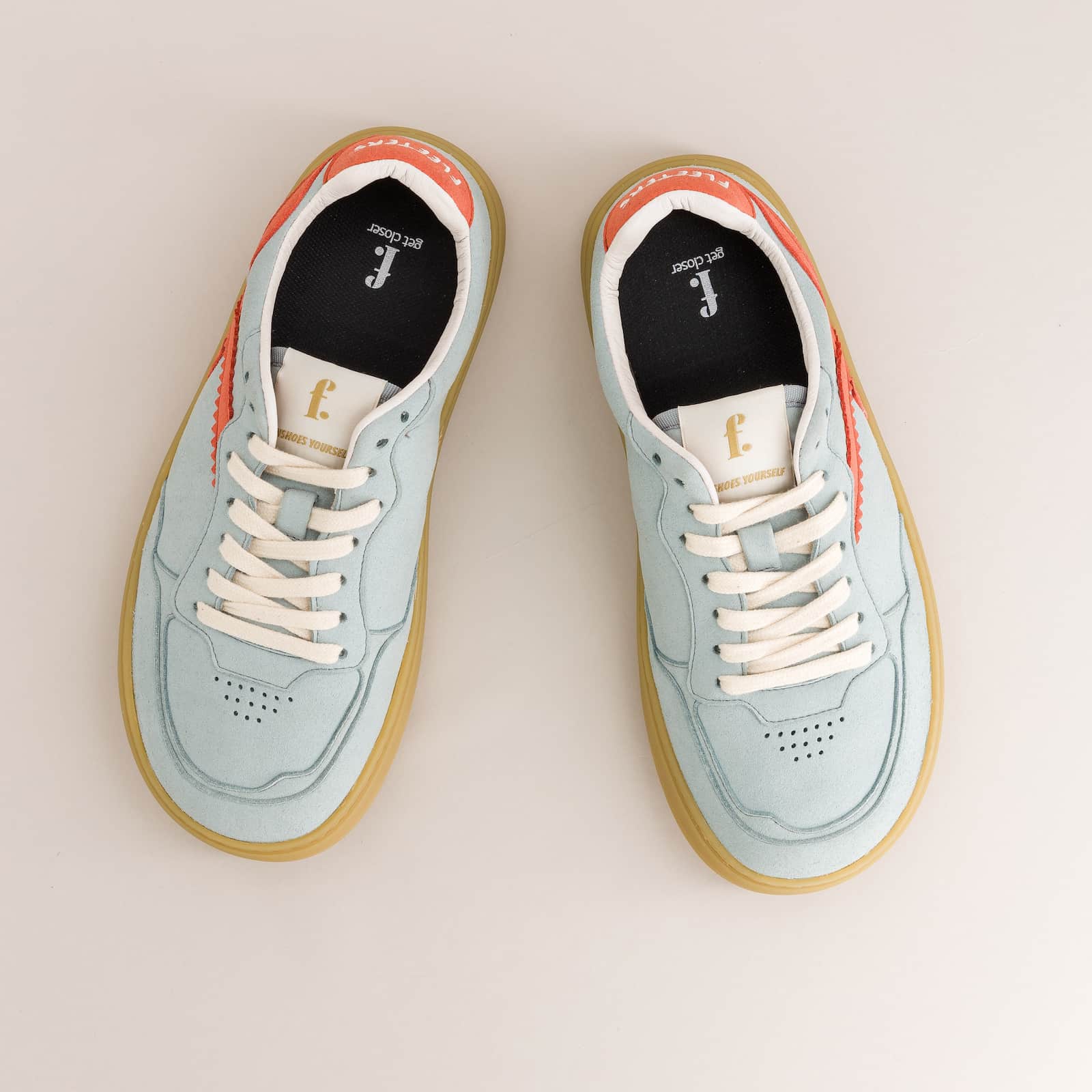 Pair of light blue barefoot sneakers with white laces on a beige background