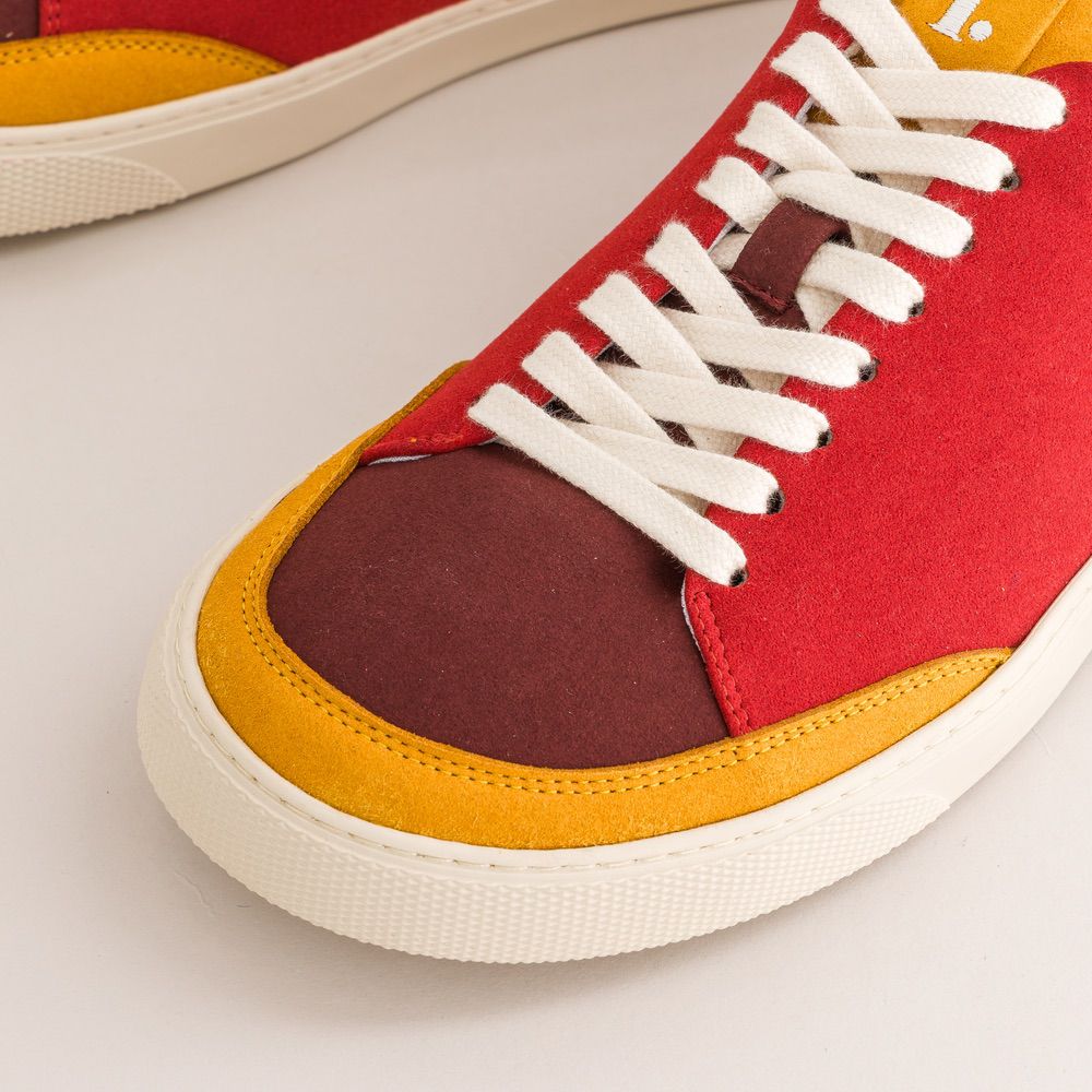 Close-up of a red, yellow, and white barefoot sneaker with white laces on a light gray background.