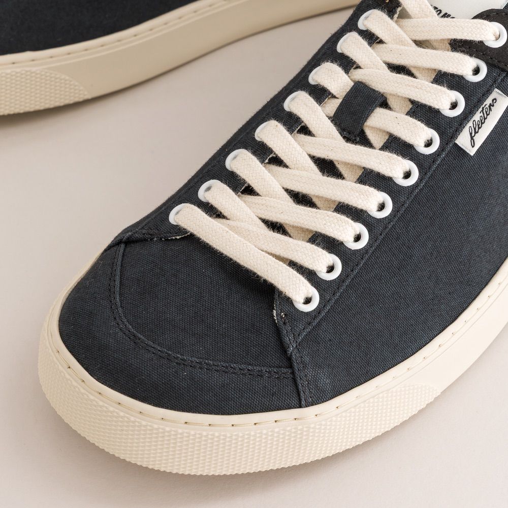 Black sneaker with white laces on a light background