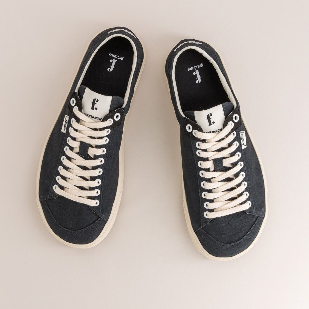 Pair of black sneakers with white laces on a light beige background