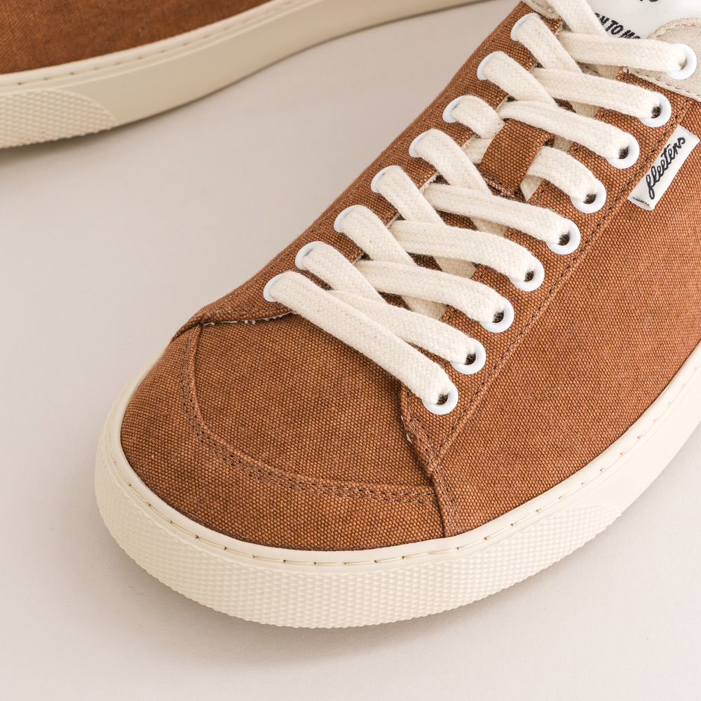 Brown canvas sneaker with white laces on a light background