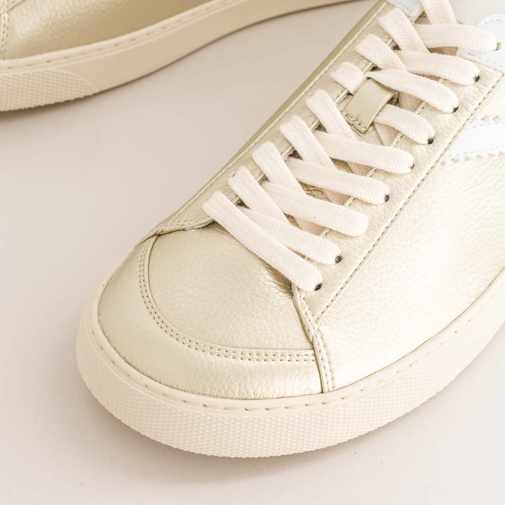 gold barefoot sneaker with white laces on a light background