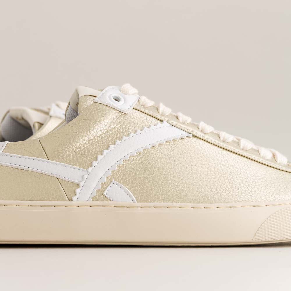 Close-up of a gold barefoot sneaker with white laces on a light gray background