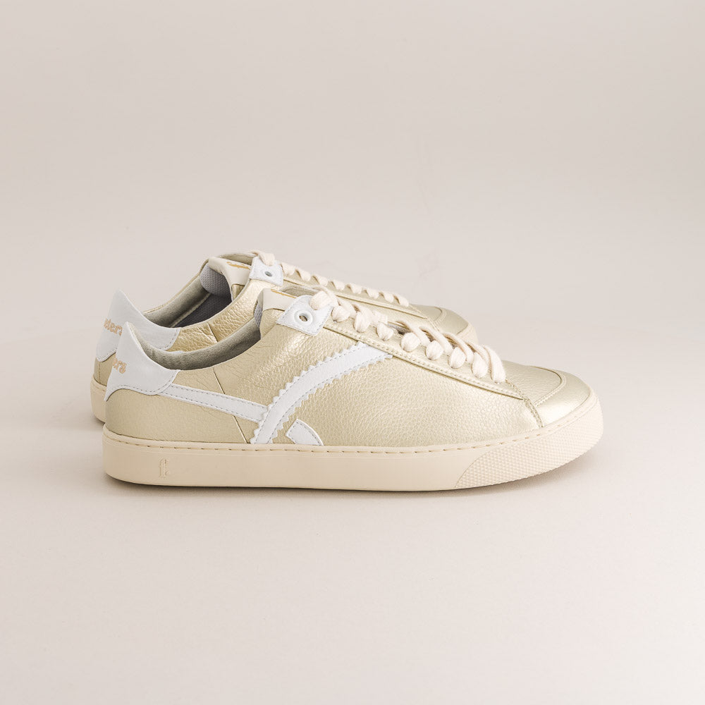 gold barefoot sneaker with white accents on a beige background