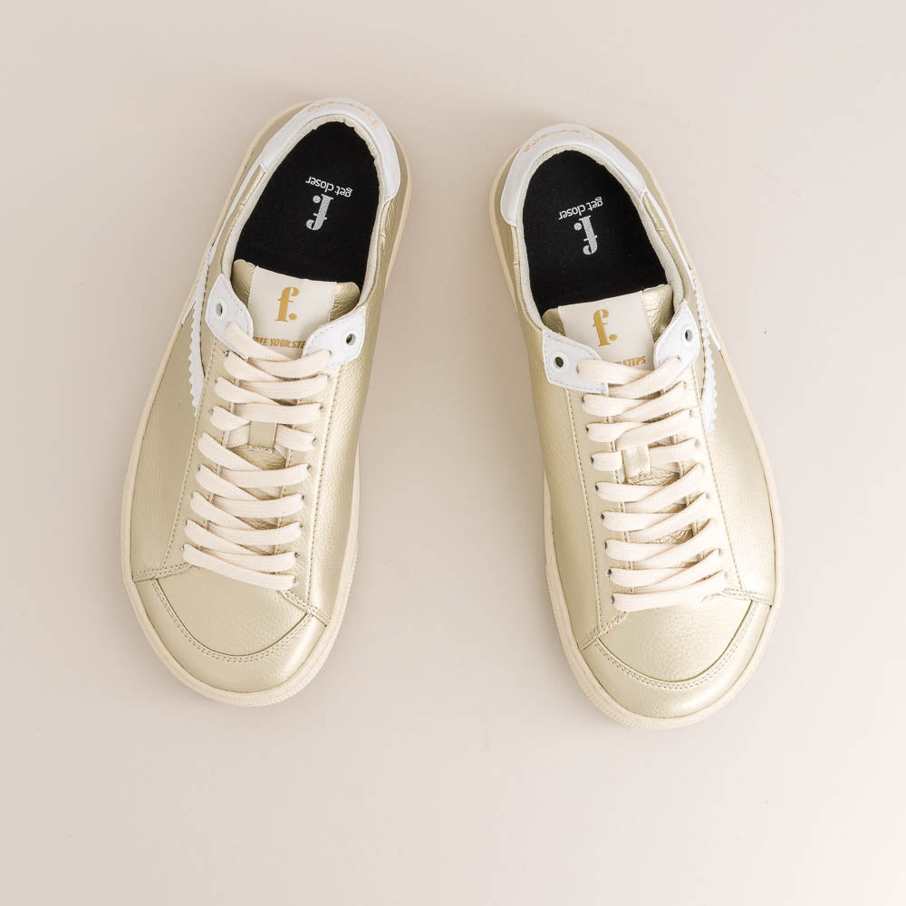 Pair of gold barefoot sneakers on a light beige background