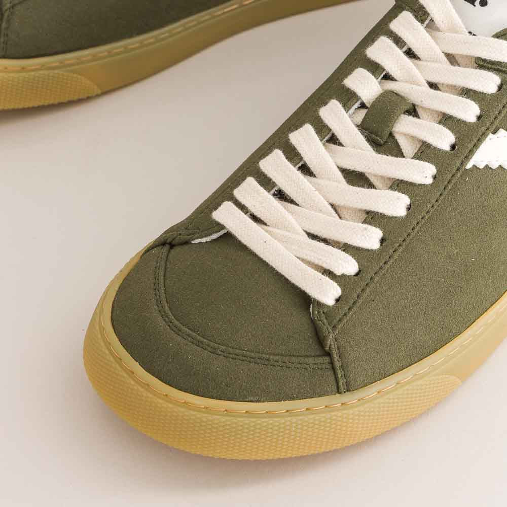 Green barefoot sneaker with white laces on a light background