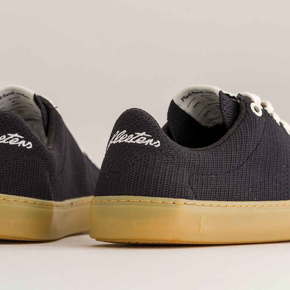 Black knit barefoot sneakers with tan soles on a light gray background