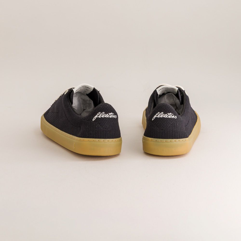 Pair of black knit barefoot sneakers with 'fleetors' branding on a light gray background