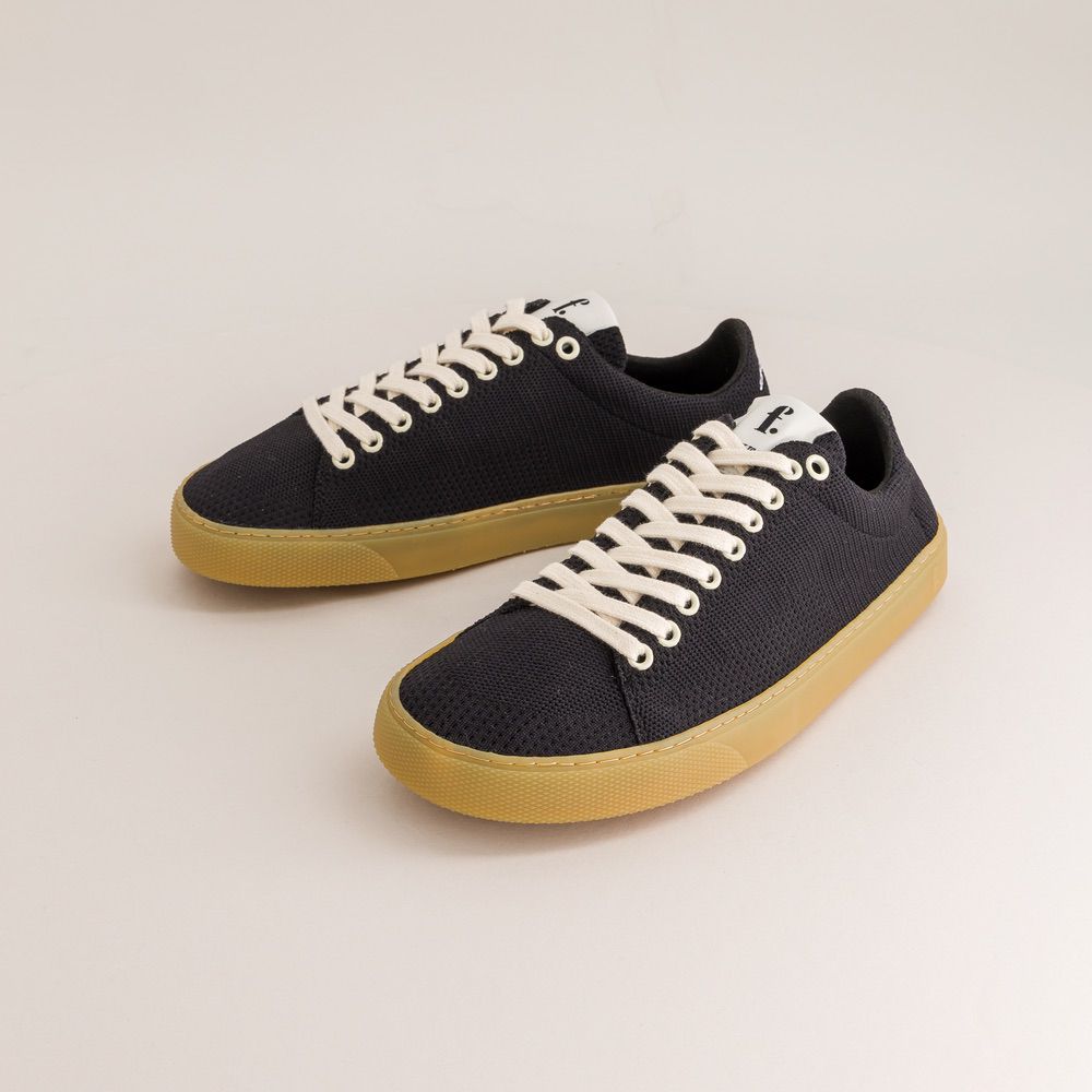 Pair of black knit barefoot sneakers with yellow soles on a light gray background