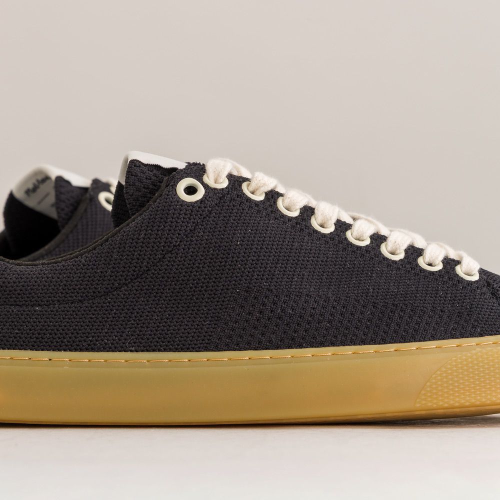 Black knit barefoot sneaker with white laces and yellow sole on a gray background