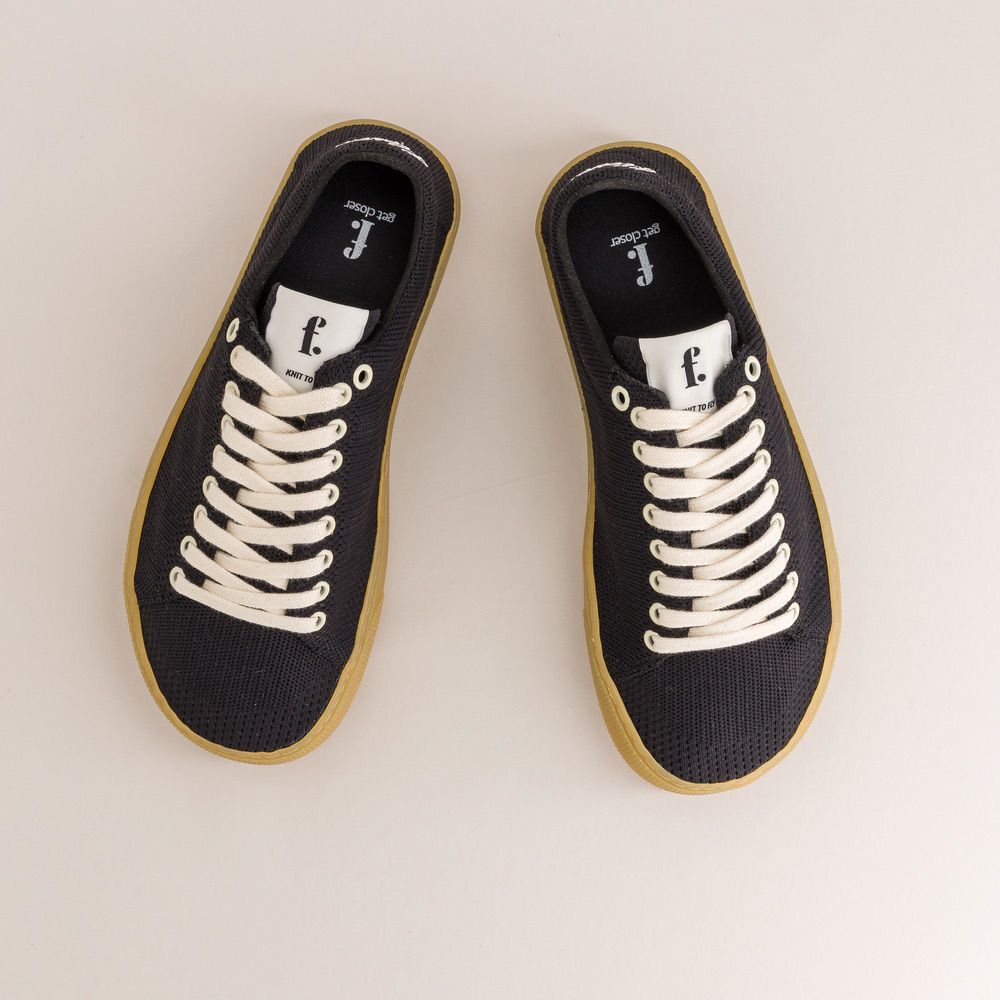 Pair of black knit barefoot sneakers with white laces on a light gray background