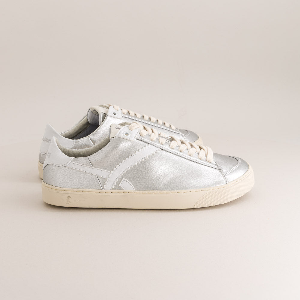 Silver barefoot sneaker with white laces on a beige background