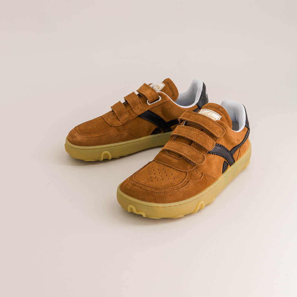 Pair of brown children's barefoot sneakers with velcro straps on a light beige background