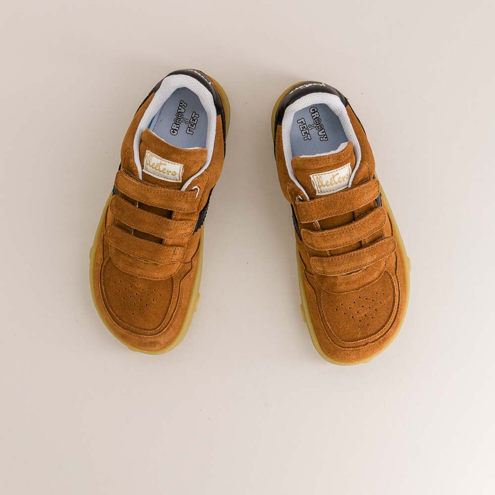 Pair of brown children's barefoot shoes with velcro straps on a light beige background