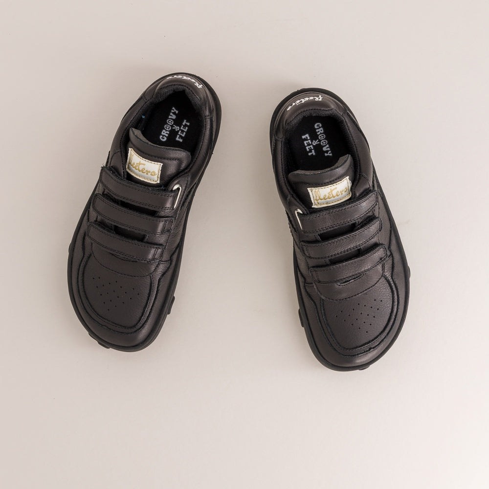 Pair of black kids barefoot shoes with velcro straps on a light gray background