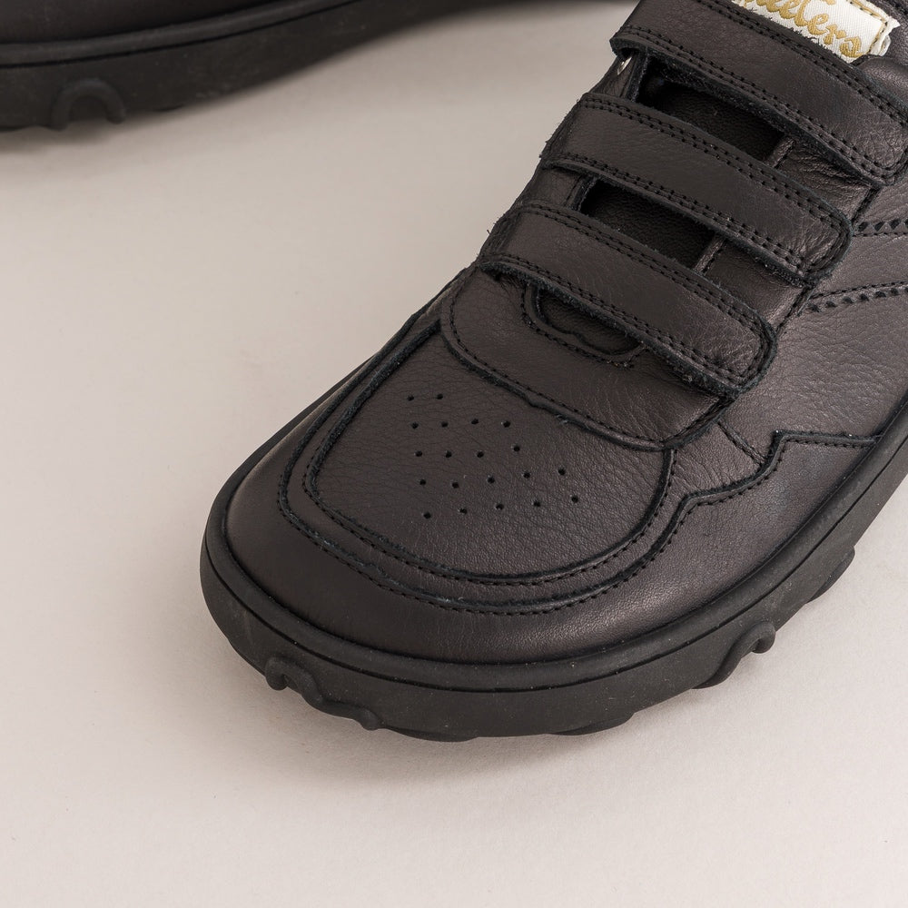 Black leather kids barefoot shoe with velcro straps on a light background