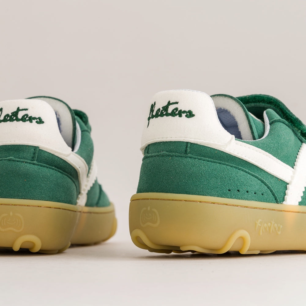 Close-up rear view of green and white sneakers with a translucent gum sole, showing the heel tab with 'Masters' script and a small pumpkin logo embossed on the sole.
