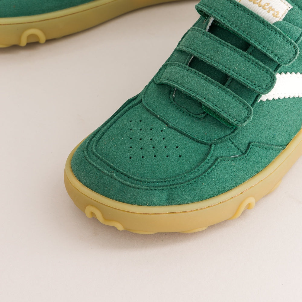 Close-up of a green children's barefoot sneaker with two hook-and-loop straps, a white side stripe, and a yellow sole on a light background.