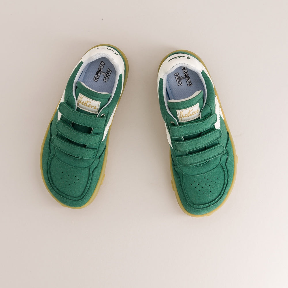 A pair of green toddler barefoot sneakers with white side stripes, green velcro straps, and gum soles, photographed from a top-down view on a light beige background.