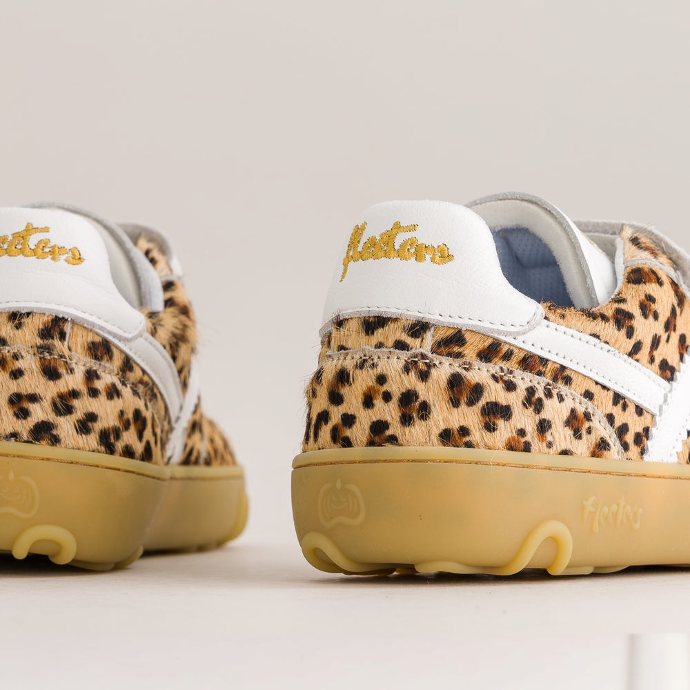 A pair of low-top sneakers shown from the back, featuring a leopard print pattern on the upper, white leather side stripes, a white heel tab with gold script embroidery, and a tan gum sole.