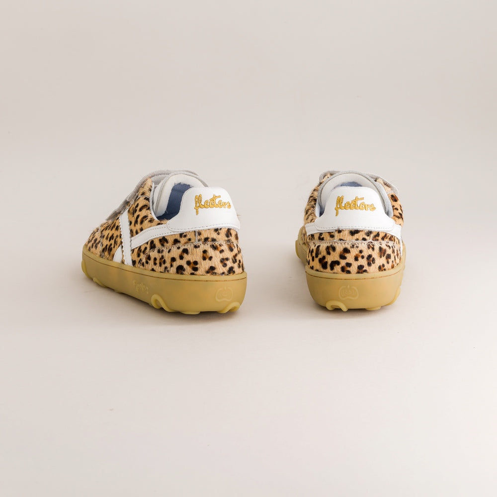 A pair of slip-on sneakers shown from the back, featuring a leopard print pattern in beige, brown, and black, a white heel tab with gold 'fleeters' text, and tan soles, set against a plain light beige background.