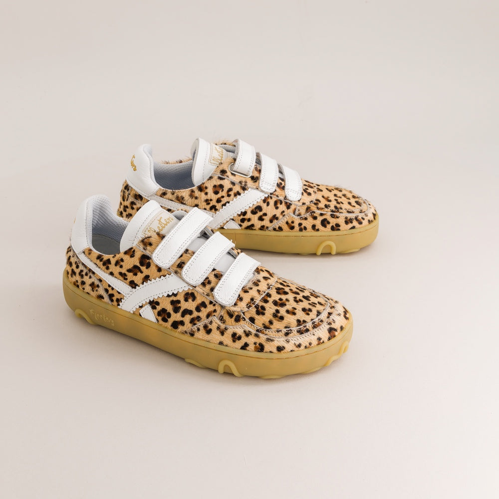 A pair of toddler barefoot sneakers with a beige and black leopard print pattern, featuring white hook-and-loop strap closures and a tan sole, shown on a light beige background.