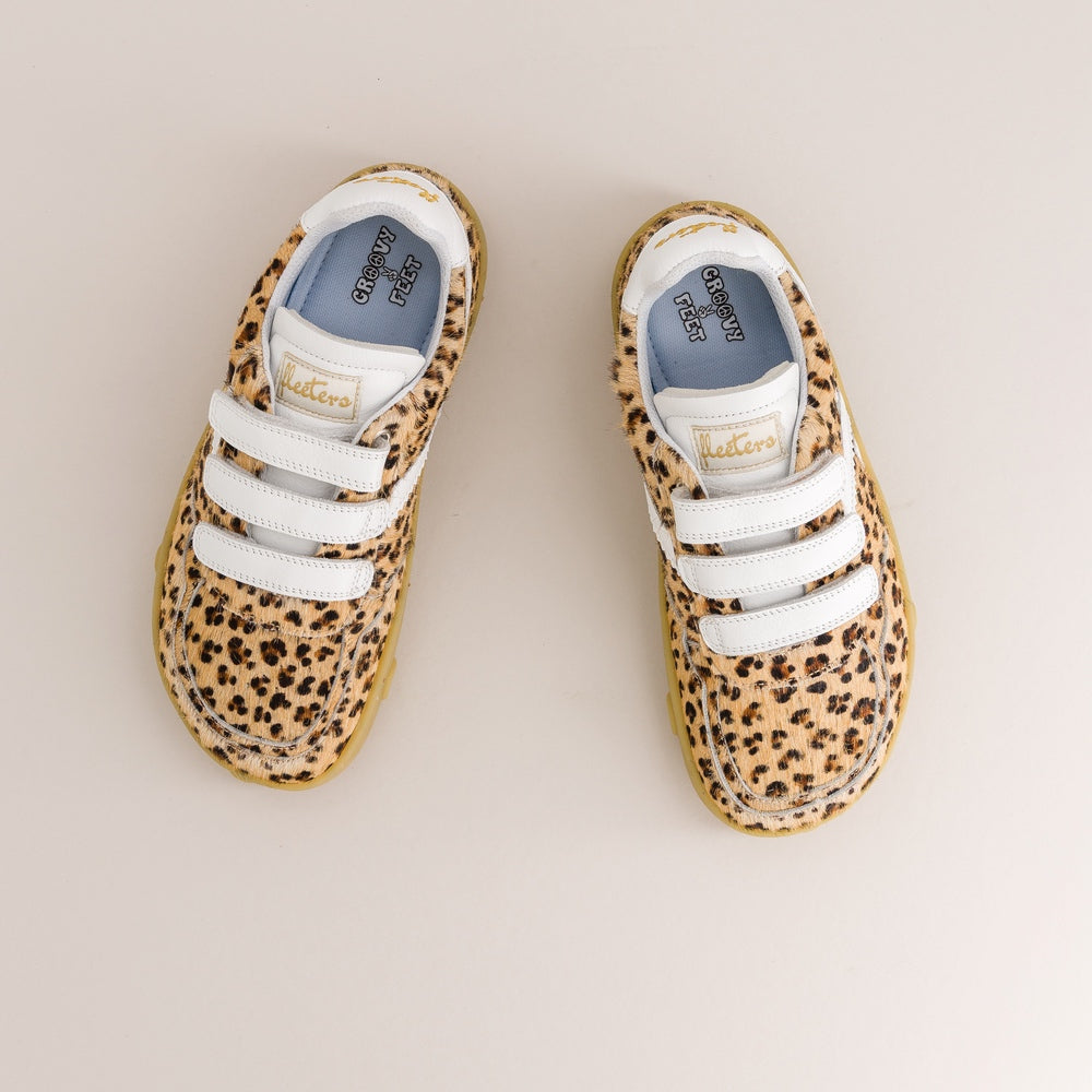 A pair of toddler barefoot sneakers with a beige and brown leopard print pattern, white hook-and-loop straps, and a light blue interior, shown from a top-down view on a light beige background.