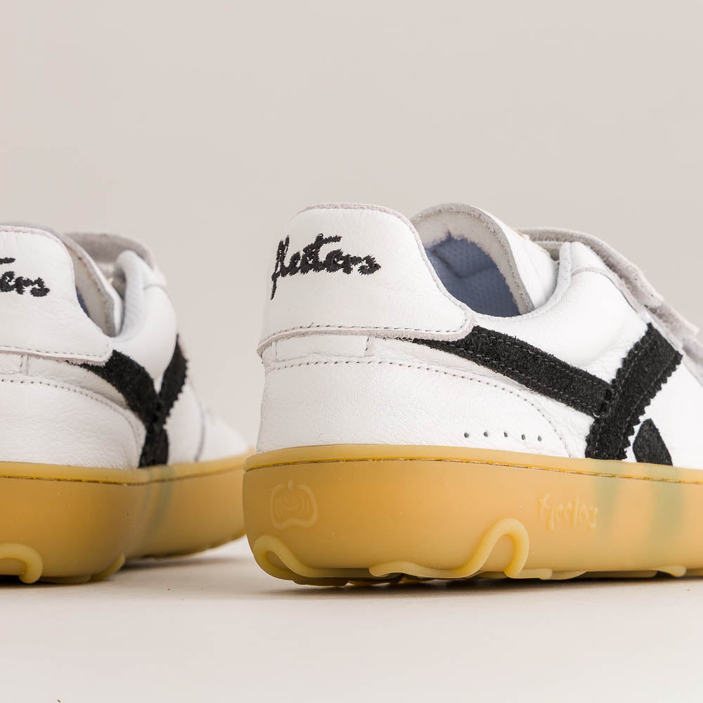 White leather sneakers with black embroidered side stripes and a translucent yellow gum sole, shown in a close-up studio shot.