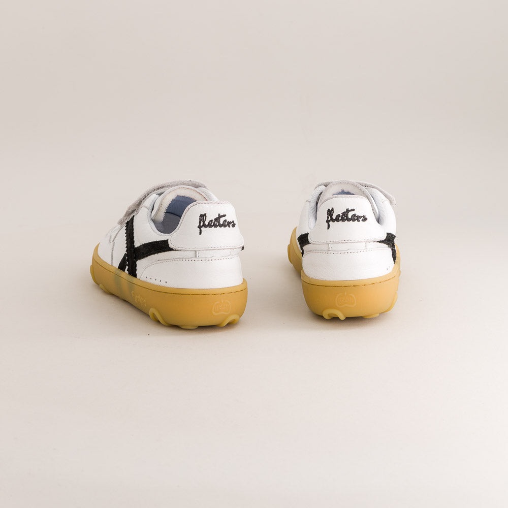 A pair of white leather sneakers with black side stripes and yellow gum soles, shown from the back on a light beige studio background. The brand name 'Fleeters' is written in black script on the heel of each shoe.