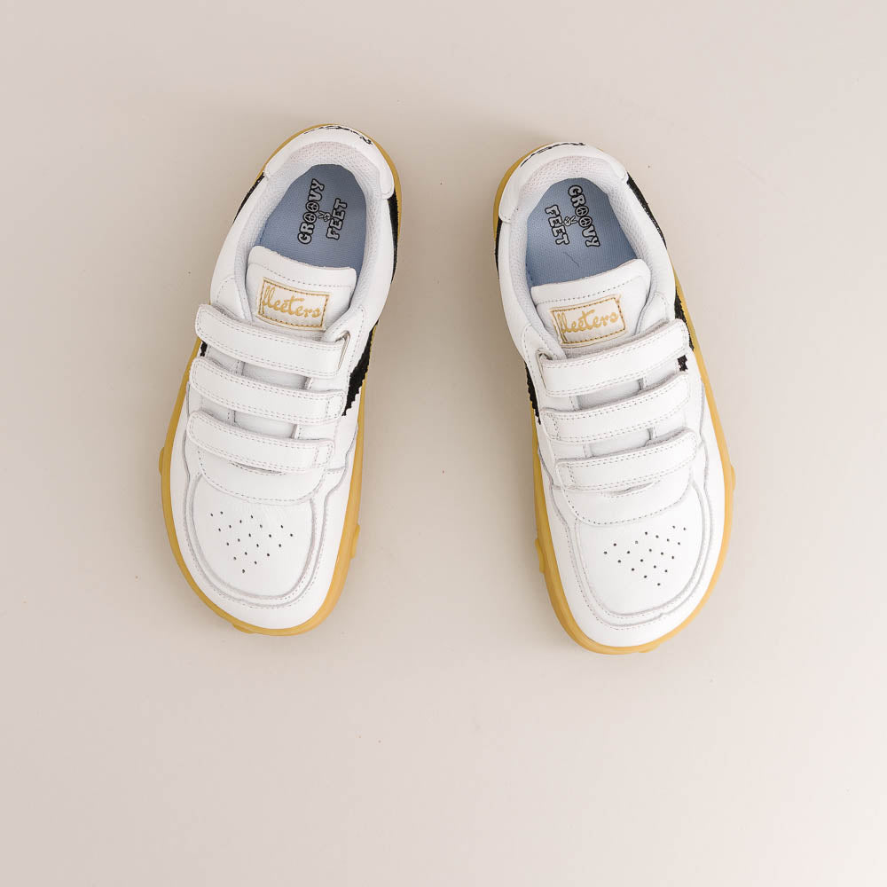 A pair of white children's barefoot sneakers with hook-and-loop straps, featuring a yellow sole and a gold 'Fleeters' brand patch on the tongue, shown from a top-down view on a light beige background.