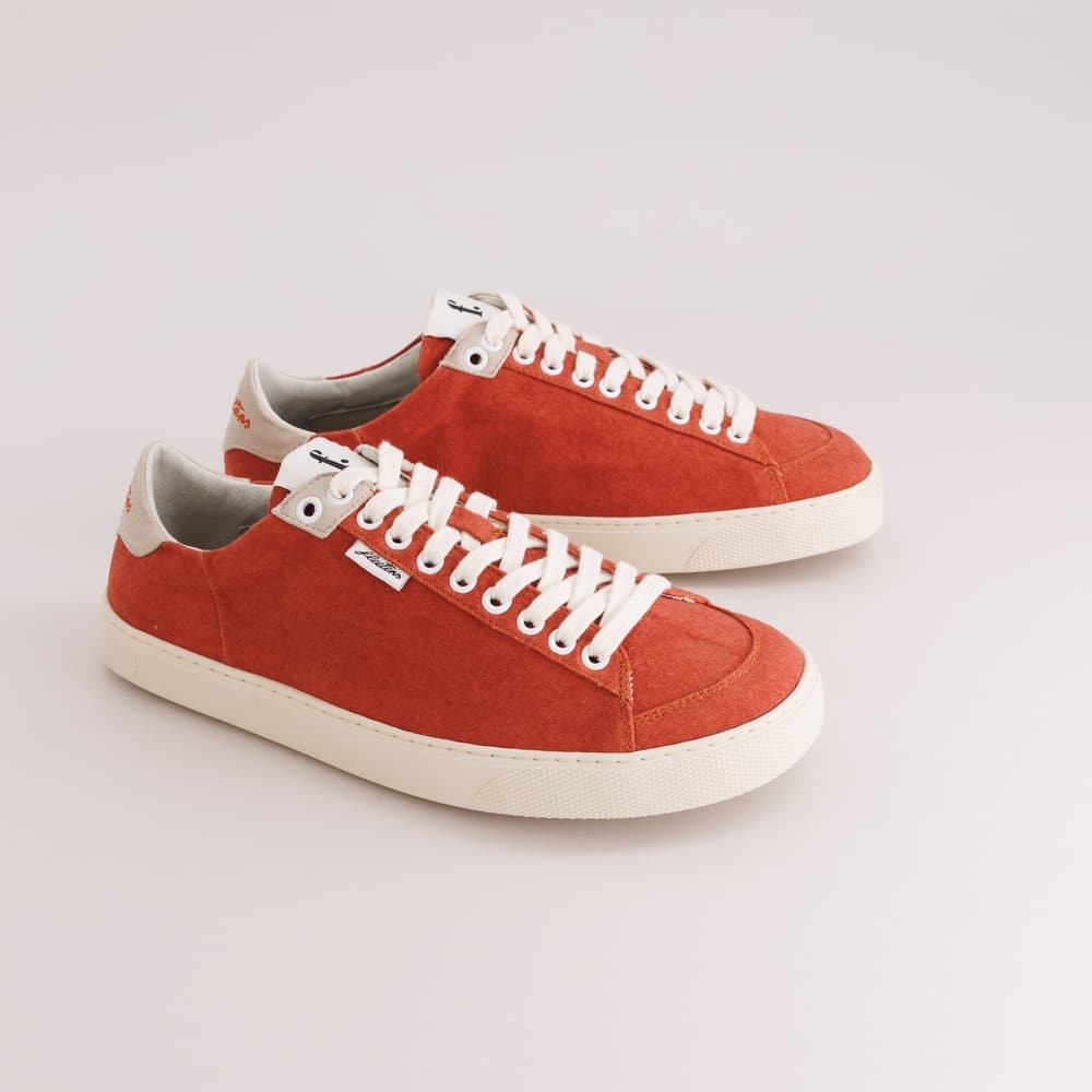 A pair of red suede low-top barefoot sneakers with white laces and white rubber soles, displayed on a light gray studio background.