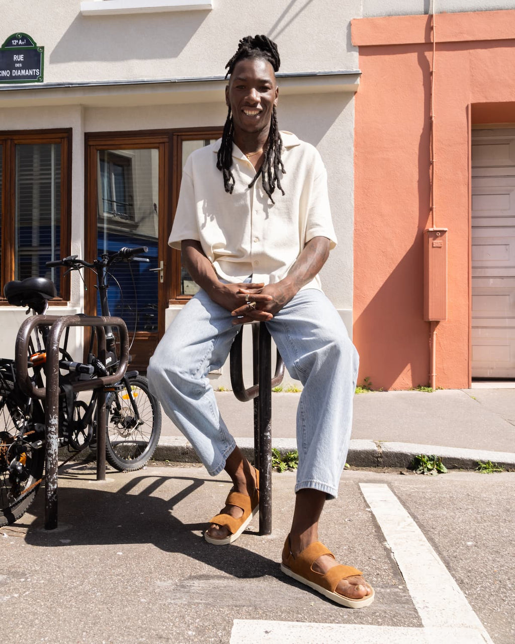 Person sitting on a bike rack in an urban setting with buildings and bicycles in the background.